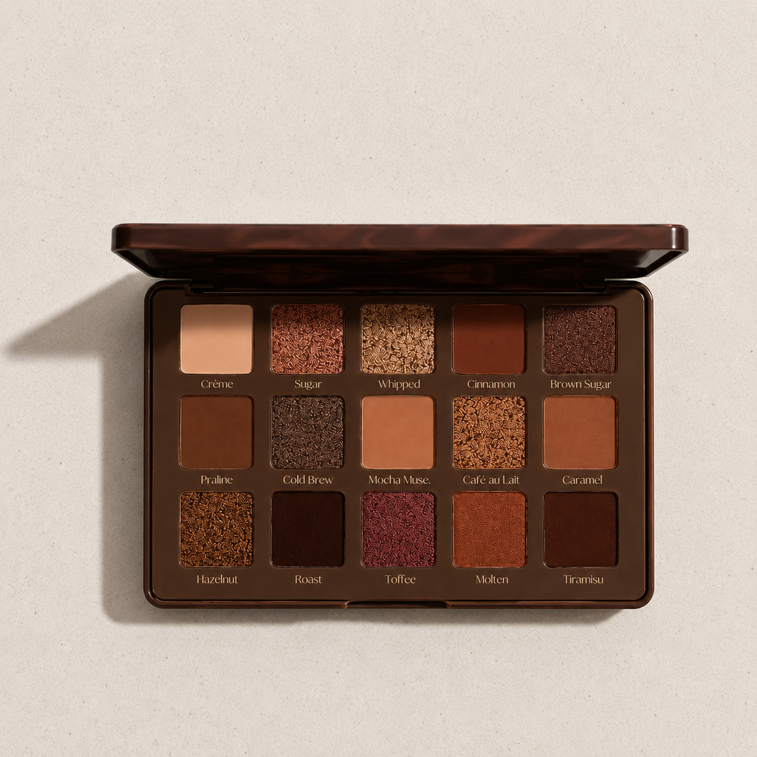 An open 12-shade eyeshadow palette with a glossy dark brown marbled lid, displayed on a textured light beige background. The shades range from cream and tan to deep browns, golds, and muted berries, each labeled with its name underneath.